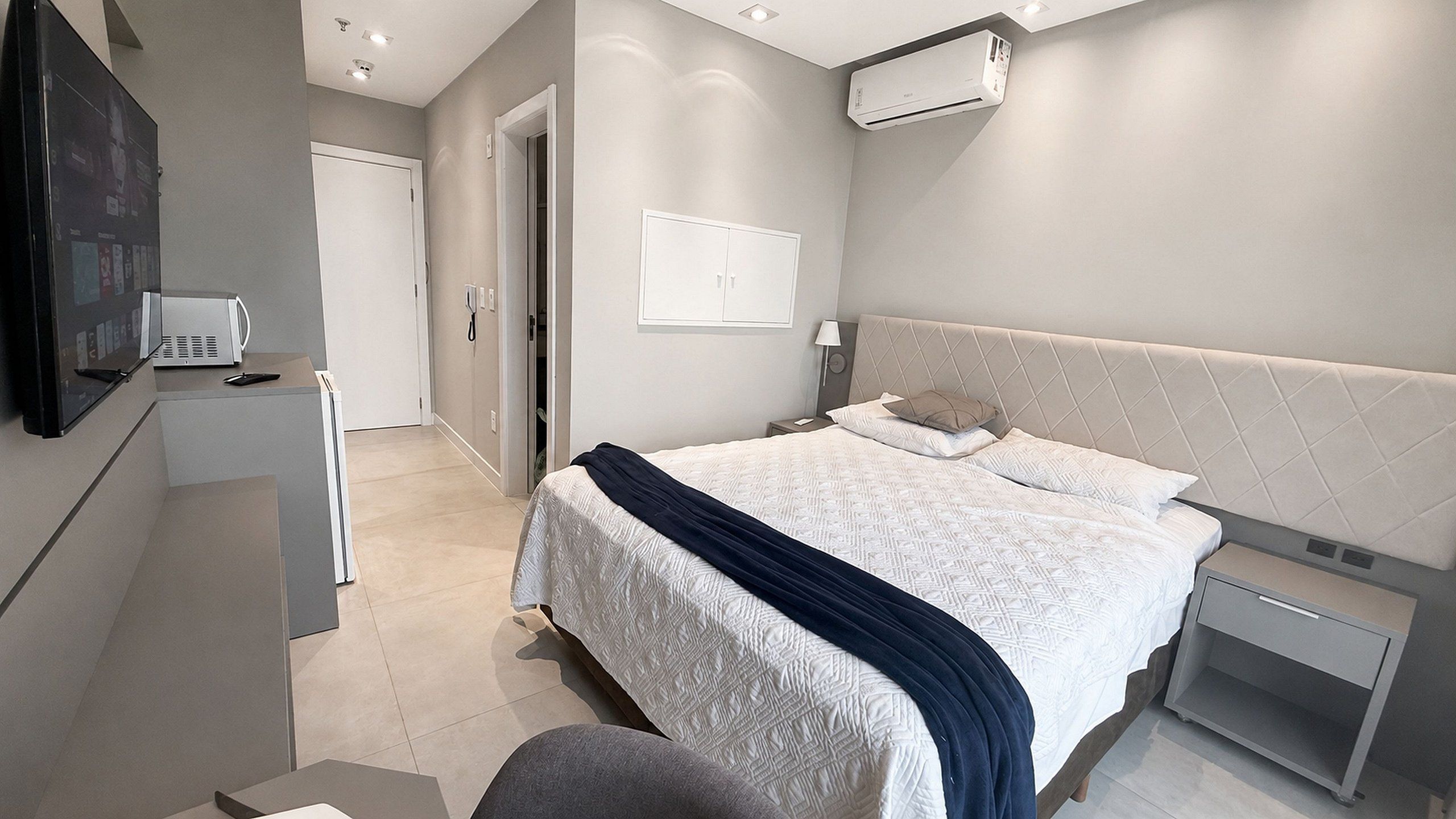Un dormitorio moderno con cama, mesitas de noche, escritorio y aire acondicionado.