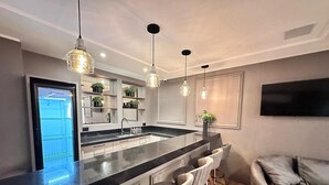 Una cocina moderna con una isla central, taburetes de bar, iluminación colgante y televisión integrada.