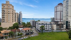 Uma área residencial costeira com edifícios altos, vista clara para o mar e um estacionamento com carros.