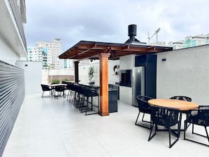 An outdoor patio area with a pergola, seating, and a refrigerator. - Manhattan Flats (Itapema)