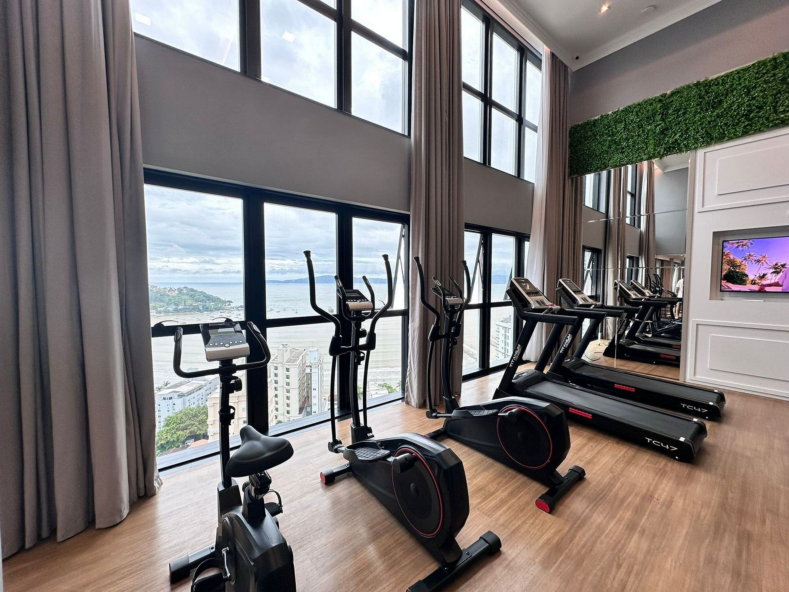 A gym with various exercise equipment, large windows, and a view of a cityscape.