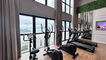 A gym with various exercise equipment, large windows, and a view of a cityscape.