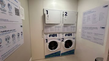 Una lavandería con dos lavadoras, numeradas 1 y 2, y carteles instructivos en las paredes.