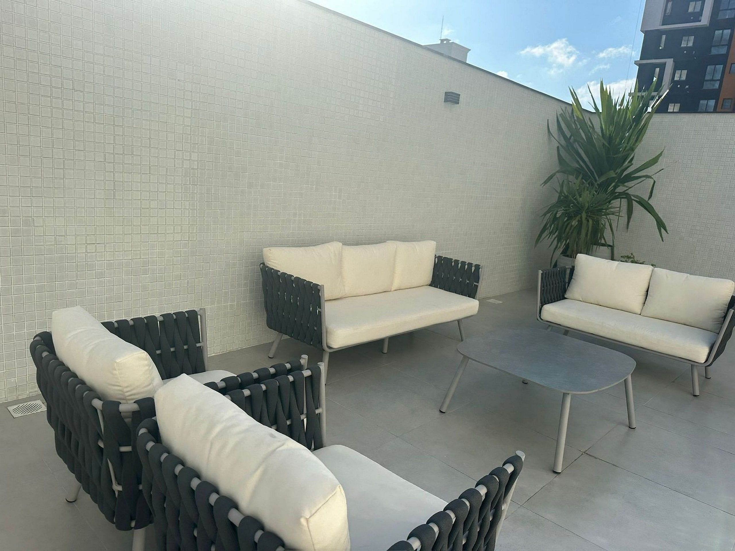 Uma área de pátio com móveis de exterior, incluindo dois sofás e duas poltronas, uma mesa pequena e um vaso de planta.