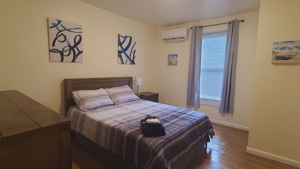 Een slaapkamer met een houten bed, een nachtkastje, een airconditioner en een raam met gordijnen.