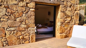 Habitación con paredes de piedra, una cama y una terraza de madera.