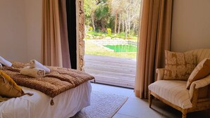 A bedroom with a bed, a chair, and a view of a garden with a pond.