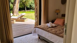 A bedroom with a bed, a nightstand, a lamp, and a view of an outdoor deck with a chair and a table.