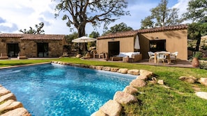 A swimming pool surrounded by stone walls, with outdoor seating and a large tree in the background.