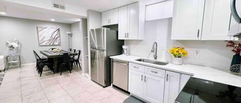 Una cocina moderna con armarios blancos, electrodomésticos de acero inoxidable y un comedor con mesa de mármol.