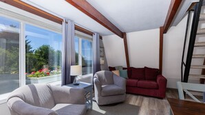 A modern living room with a large window, a red sofa, two armchairs, and a wooden staircase.