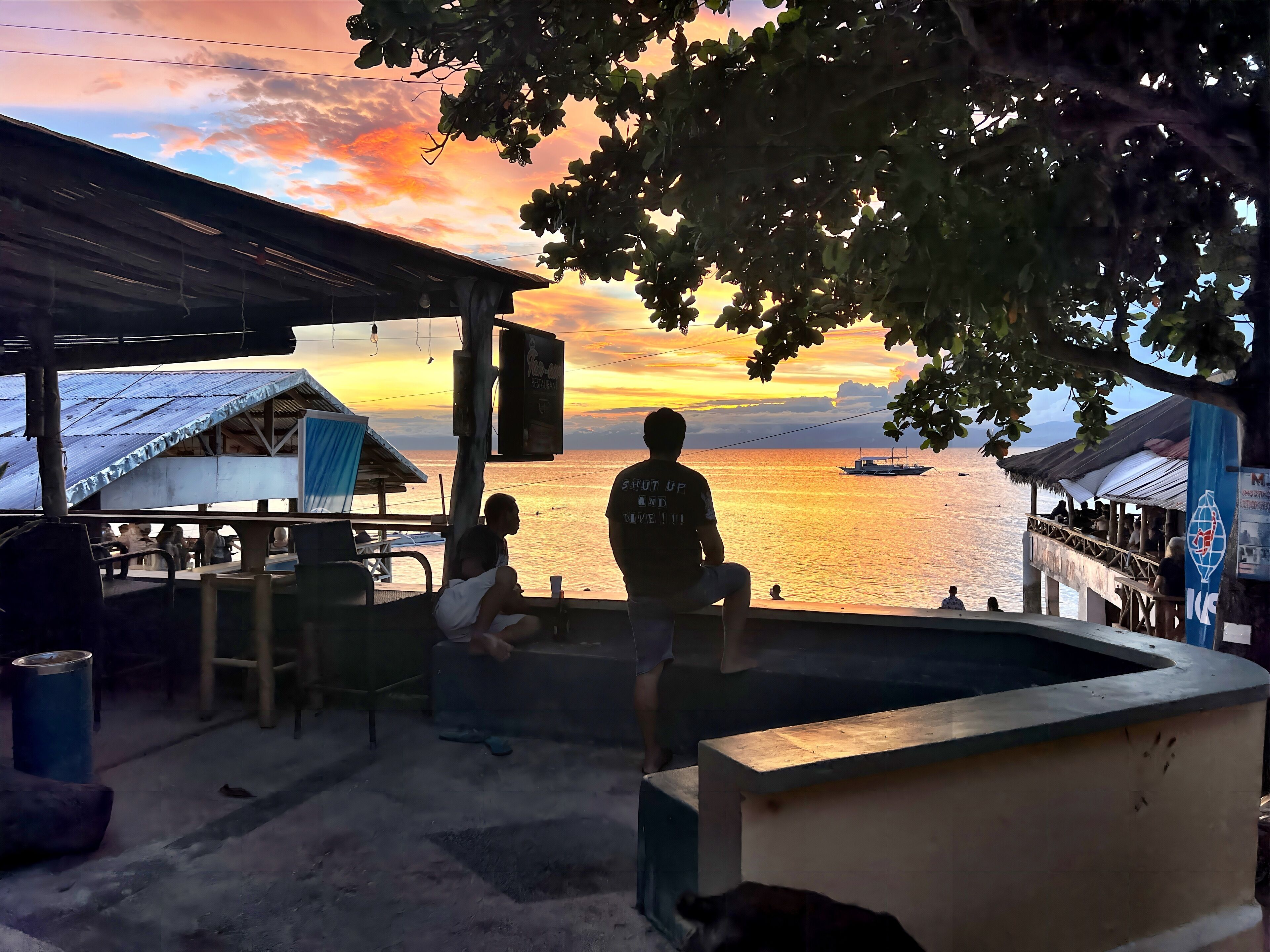 A coastal scene with a sunset view, a pier with people, and a restaurant sign.
