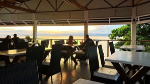 An outdoor dining area with tables and chairs, overlooking a body of water during sunset. - Beautiful, spacious, resort on the beach front. (Moalboal)