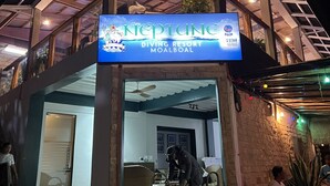 A Neptune Diving Resort Moalboal entrance with a sign, a covered outdoor area, and a person in diving gear. - Beautiful, spacious, resort on the beach front. (Moalboal)