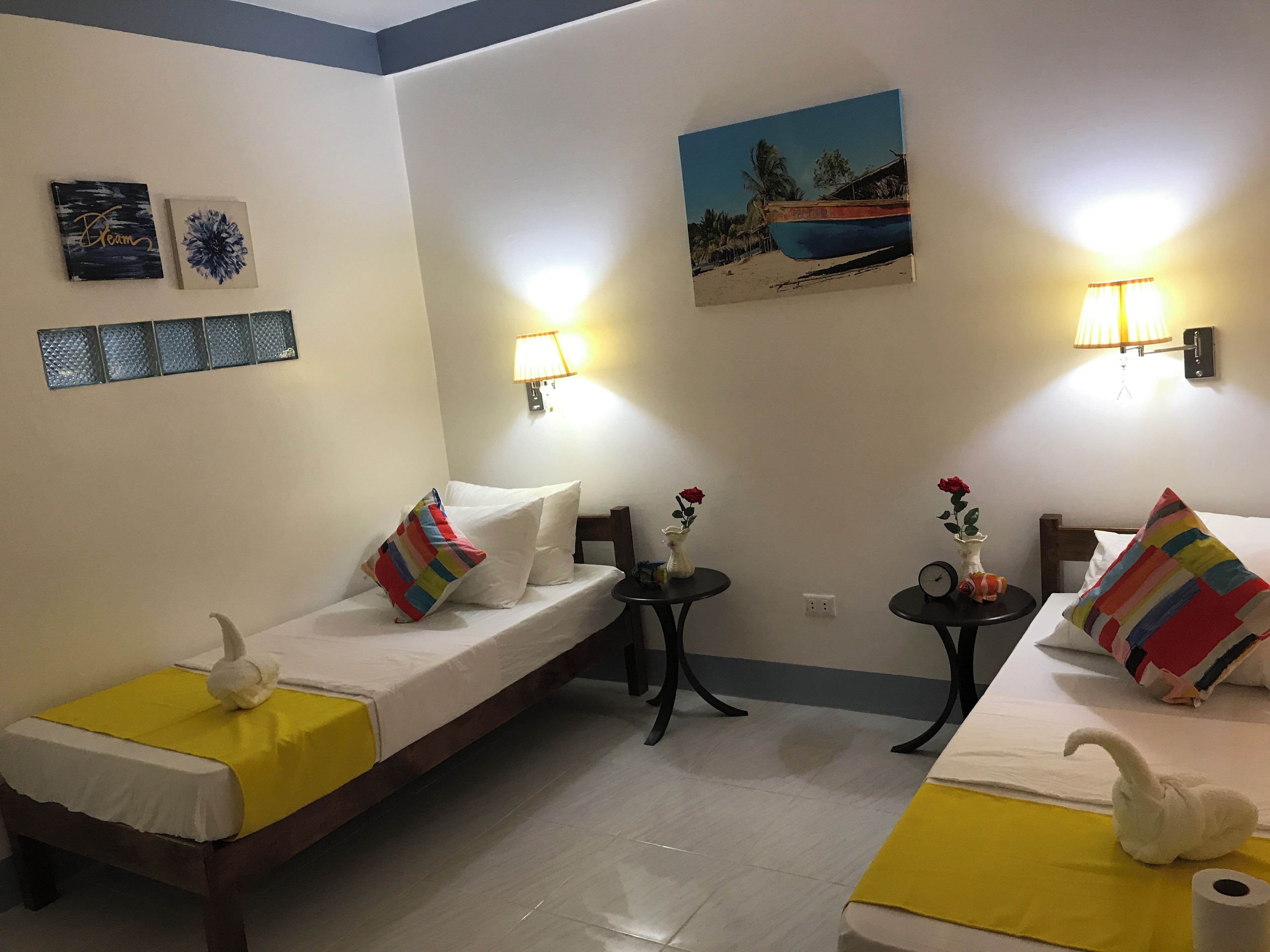Una camera d'albergo con due letti singoli, un tavolino e una lampada fissata al muro.