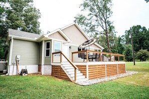 Ein zweistöckiges Haus mit einer Holzterrasse, einer Treppe und einer Terrasse mit Gartenmöbeln.