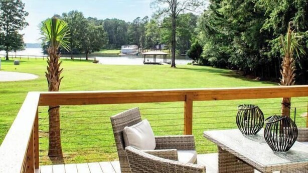 A wooden deck with wicker furniture and a glass table, overlooking a grassy area with trees and a distant view of a house. - Sunset Oasis|PrivateDock|Sleeps8 (Chappells)