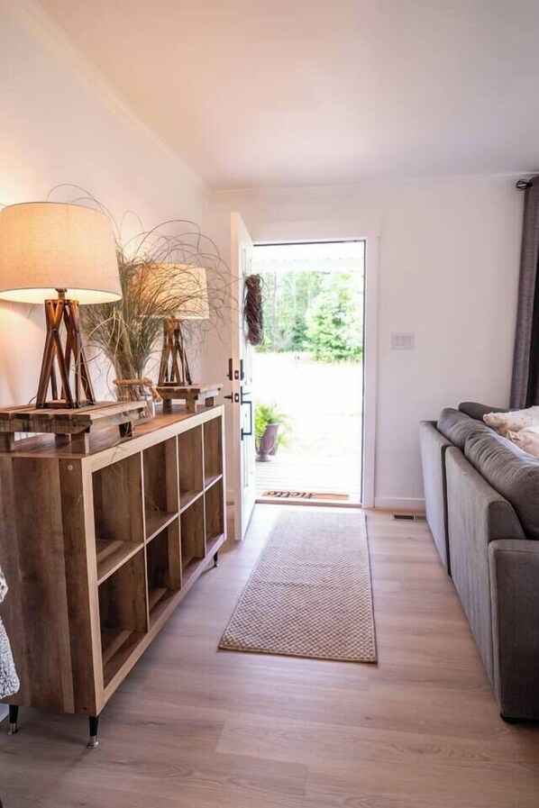 A modern living room with a wooden console table, a grey sofa, and a large window with a view of greenery.