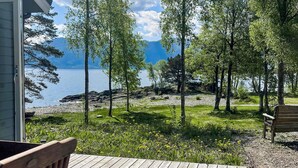 Eine Holzterrasse mit einer Bank, mit Blick auf einen See mit Bäumen und einer felsigen Uferlinie.