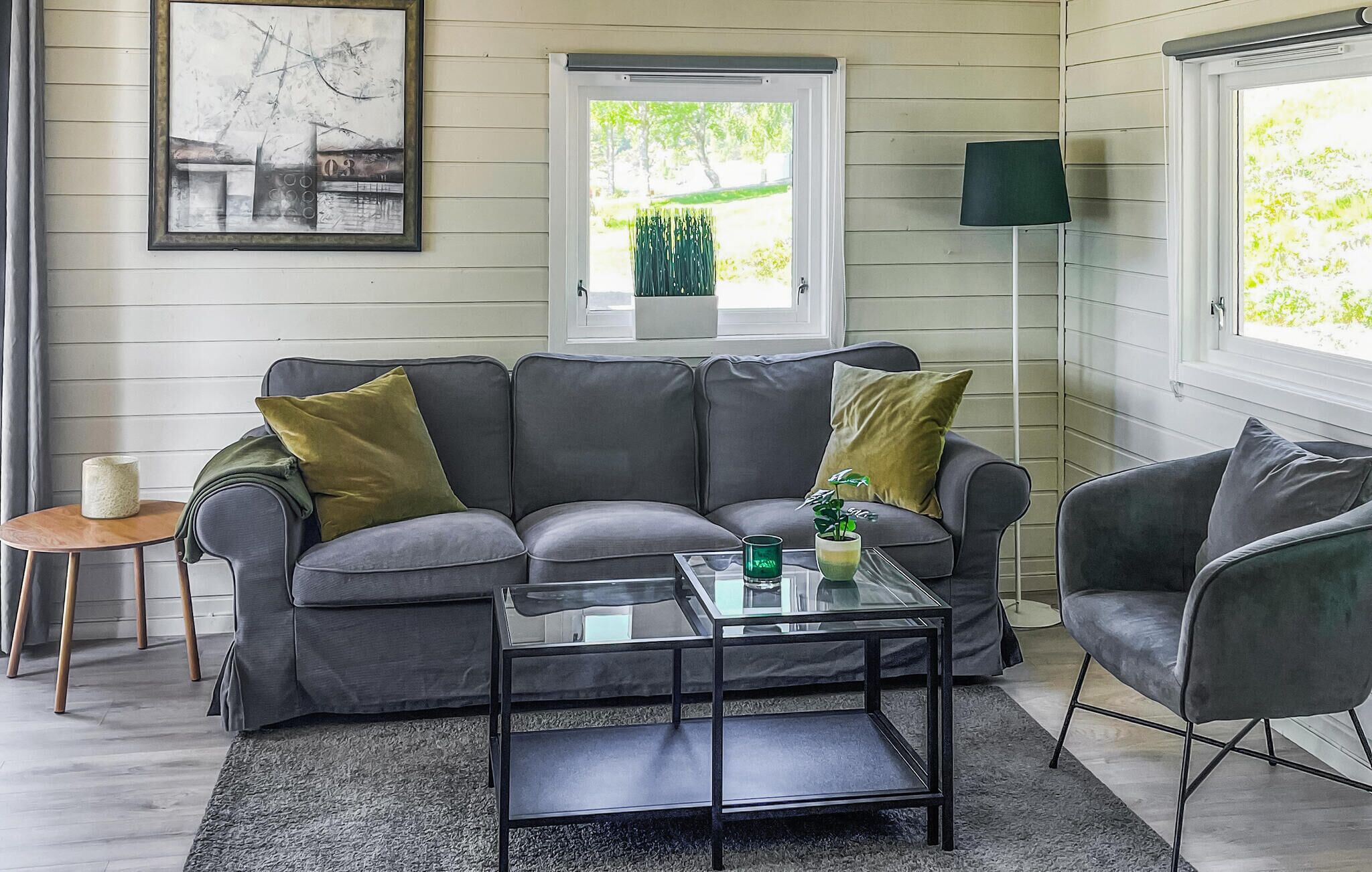 En moderne stue med en grå sofa, et glasbord og en grøn lampe.