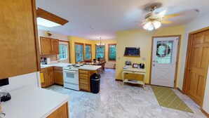 A kitchen with wooden cabinets, a white stove, and a dining area with a chandelier. - Brookside Cottage In Hocking Hills (Rockbridge)