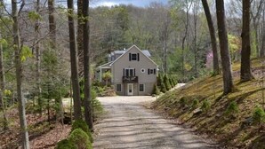 A two-story house with a front porch, surrounded by a forested area. - Brookside Cottage In Hocking Hills (Rockbridge)
