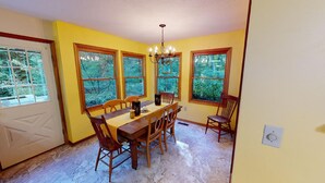 A dining room with a wooden table and chairs, large windows with a view of greenery, and a chandelier. - Brookside Cottage In Hocking Hills (Rockbridge)