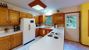 A kitchen with wooden cabinets, a refrigerator, a stove, and a window with a view of trees. - Brookside Cottage In Hocking Hills (Rockbridge)