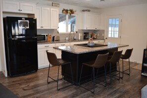 A kitchen with white cabinets, a black refrigerator, a granite countertop, and four bar stools.