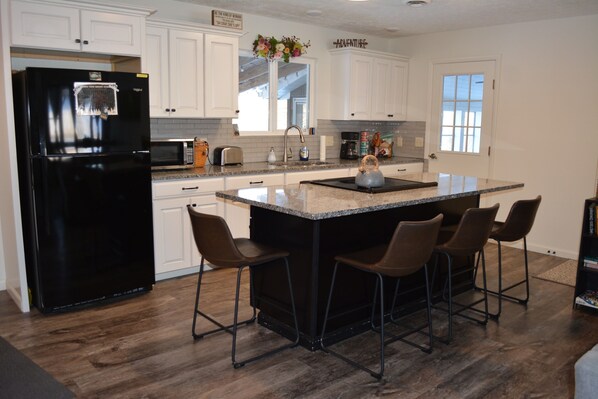 A kitchen with white cabinets, a black refrigerator, a granite countertop, and four bar stools.