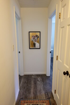 Un couloir avec un tableau encadré au mur, un tapis à l’entrée et une porte sur la droite.