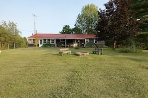 A house with a red roof, a porch with outdoor seating, and a grassy yard.