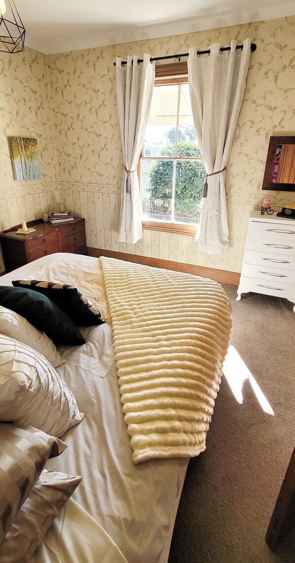 A bedroom with a bed, a nightstand, a dresser, and a window with curtains.