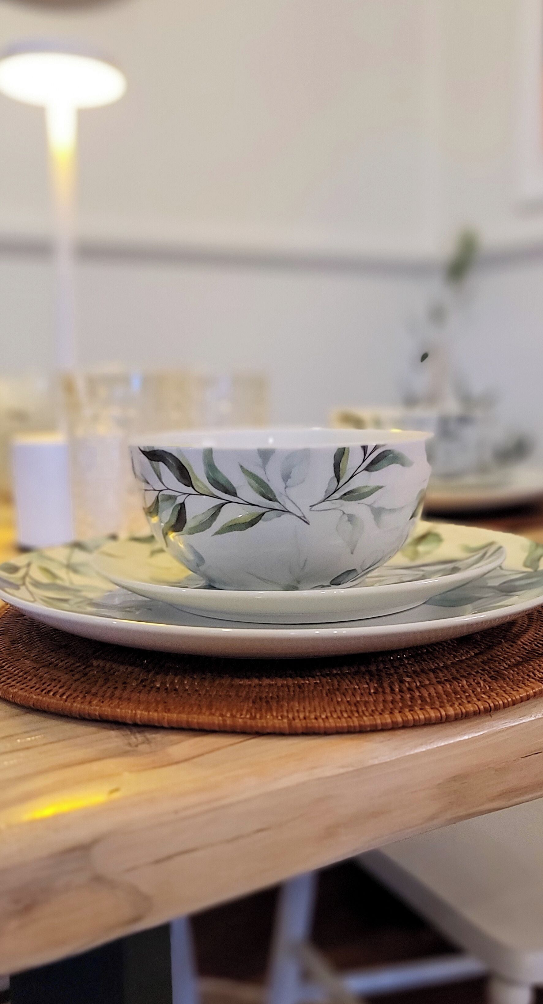 A table with a white bowl on a plate, a woven placemat, and a blurred background.