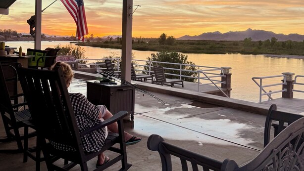 Un espacio de estar al aire libre techado con vista a un lago y montañas al atardecer.