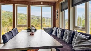A dining area with a long table and cushioned seating, large windows with a view of a hilly landscape. - Cozy home in Hovden i Setesdal - with jacuzzi (Hovden i Setesdal)