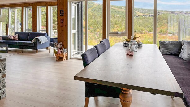 A spacious room with a large dining table, a blue sofa, and a view of a forested landscape through large windows. - Cozy home in Hovden i Setesdal - with jacuzzi (Hovden i Setesdal)