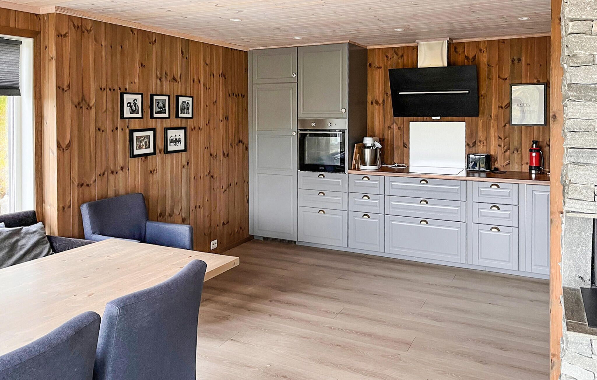 A modern kitchen with wooden paneling, grey cabinets, and a dining area with a table and chairs.