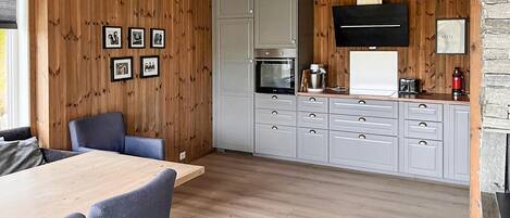 A modern kitchen with wooden paneling, grey cabinets, and a dining area with a table and chairs.