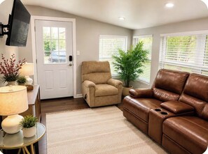 A living room with a beige armchair, a brown leather sofa, a small table with a lamp, and a potted plant.