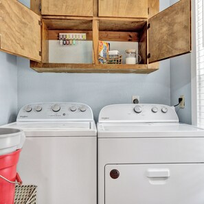 Uma lavanderia com duas máquinas de lavar Whirlpool brancas, um armário de madeira acima e um balde vermelho com um esfregão.