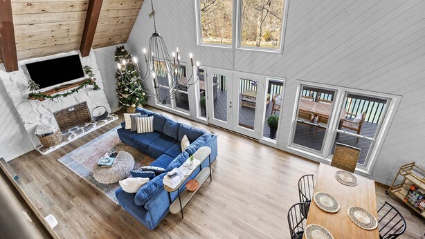 A spacious loft with a high ceiling, a cozy blue sectional sofa, a fireplace, and large windows offering views of the outdoors.