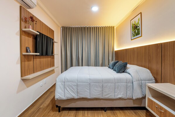 A bedroom with a bed, built-in shelves, a wall-mounted TV, and a ceiling light.