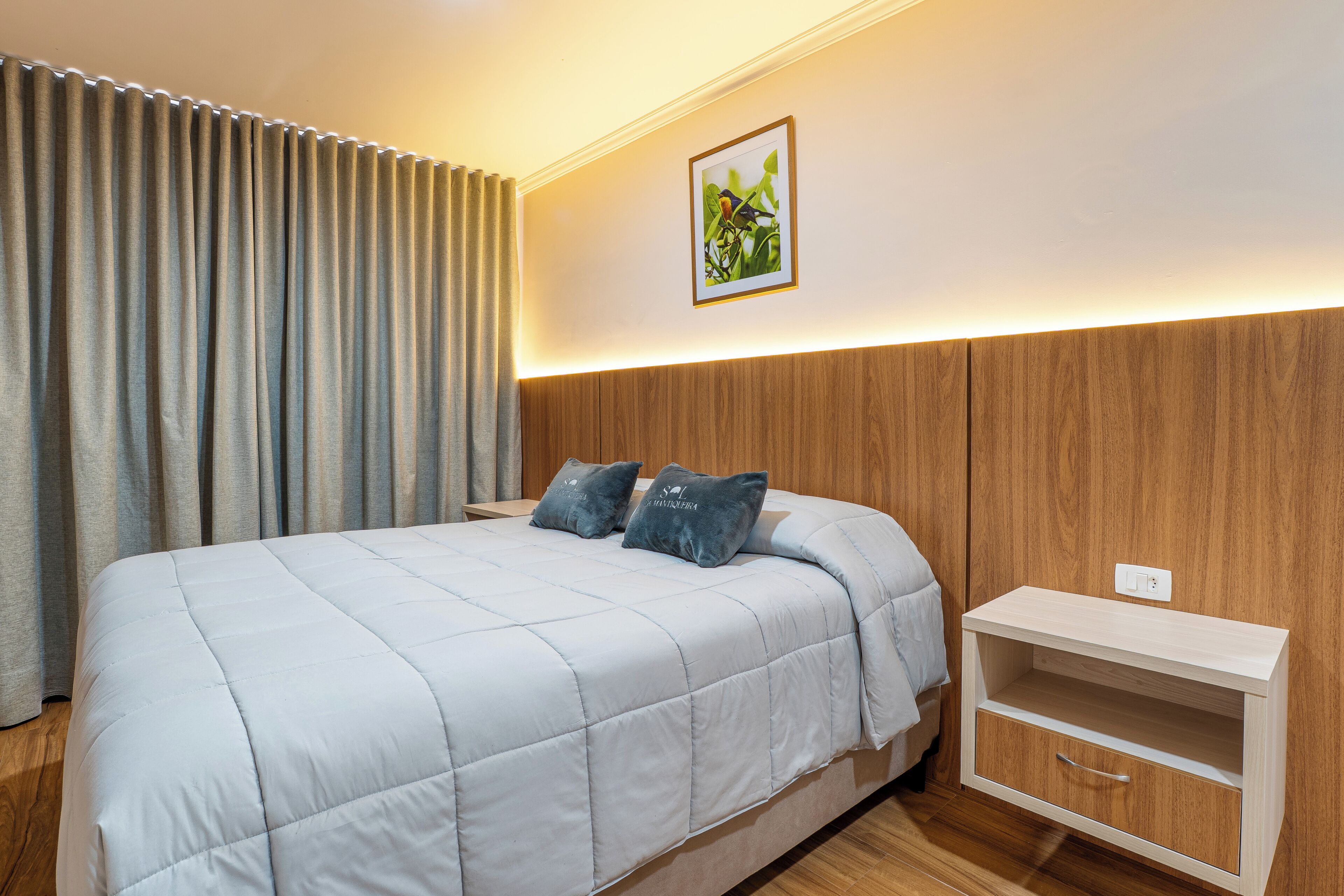 A neatly made bed with a light-colored duvet, a bedside table with a drawer, and a wall-mounted light fixture.