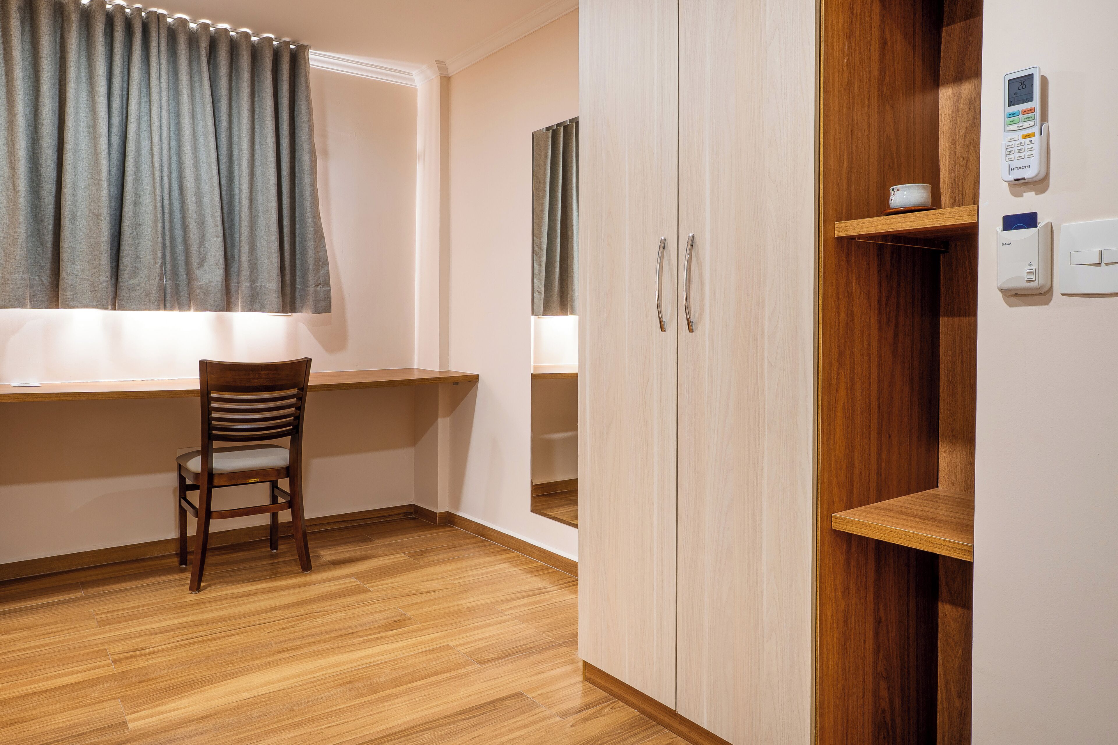 A room with a wooden floor, a desk with a chair, a wardrobe, and a window with curtains.