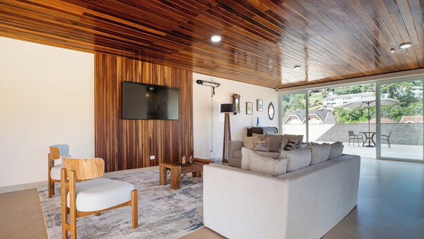 A modern living room with a wooden ceiling, a flat-screen TV, a sofa, a chair, and a coffee table.