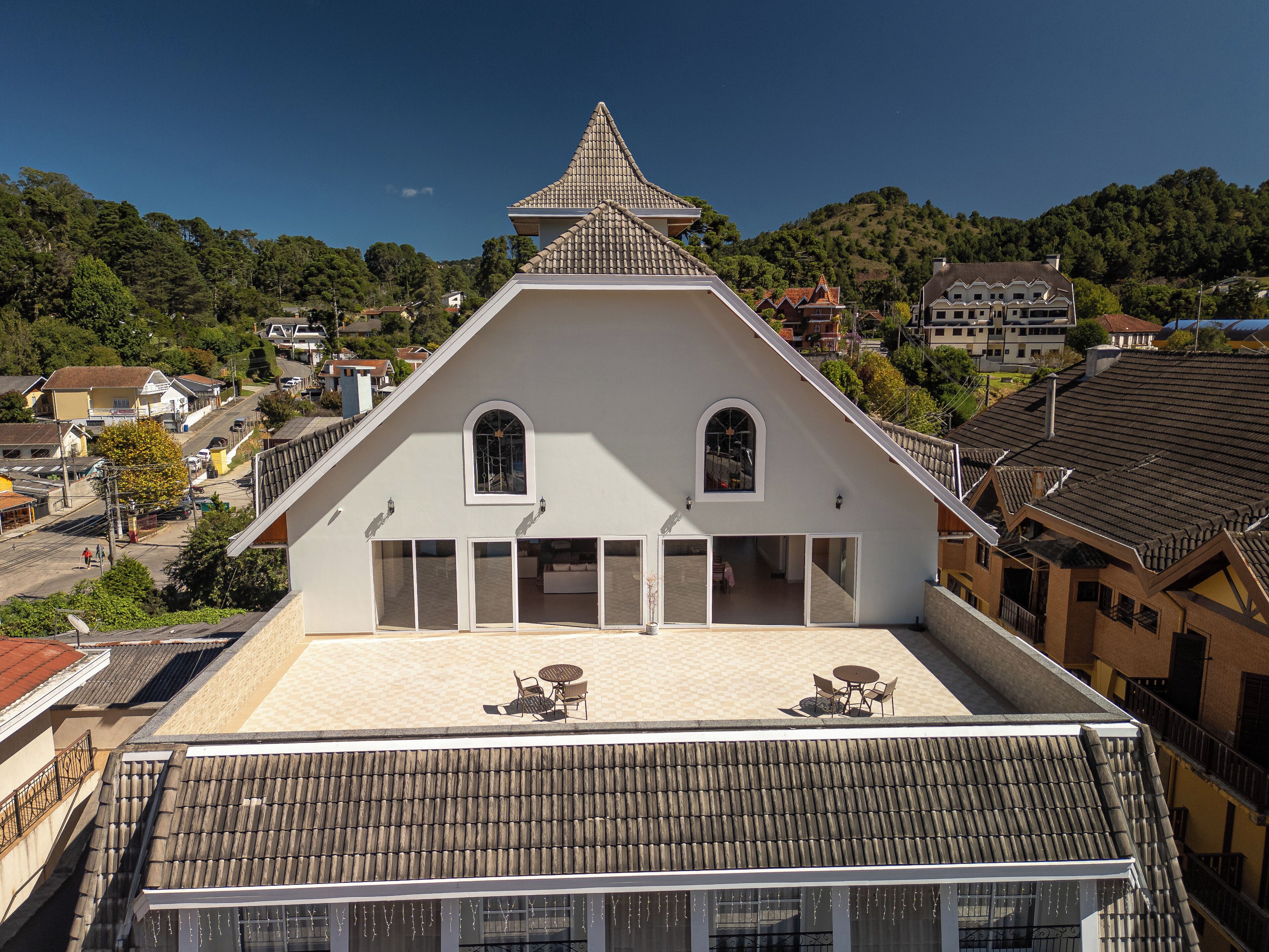 A building with a steep roof, a balcony with outdoor seating, and a view of the surrounding neighborhood.
