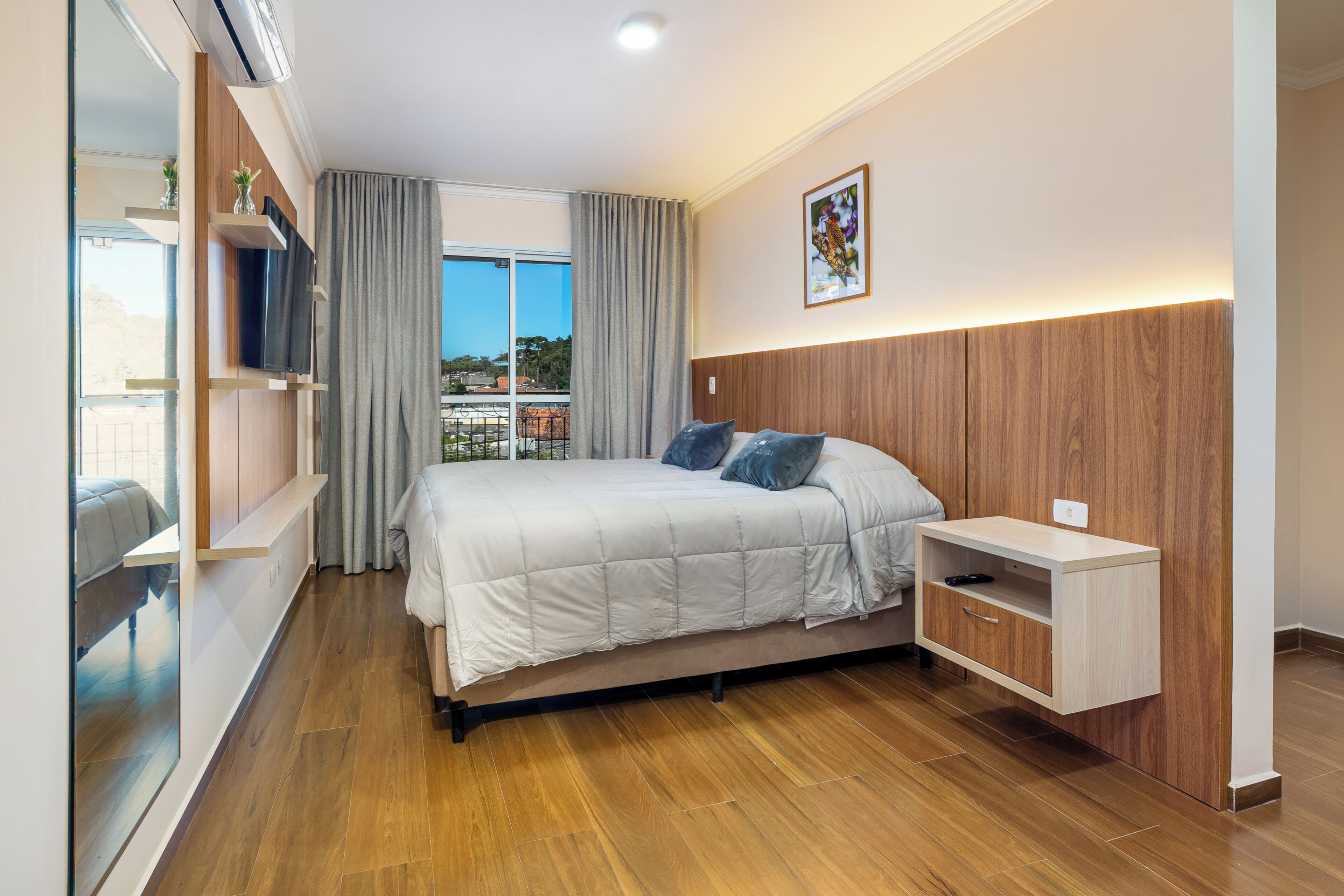 Une chambre à coucher comprenant un lit, une télévision, une table de chevet, une fenêtre avec des rideaux et une vue sur l’extérieur.