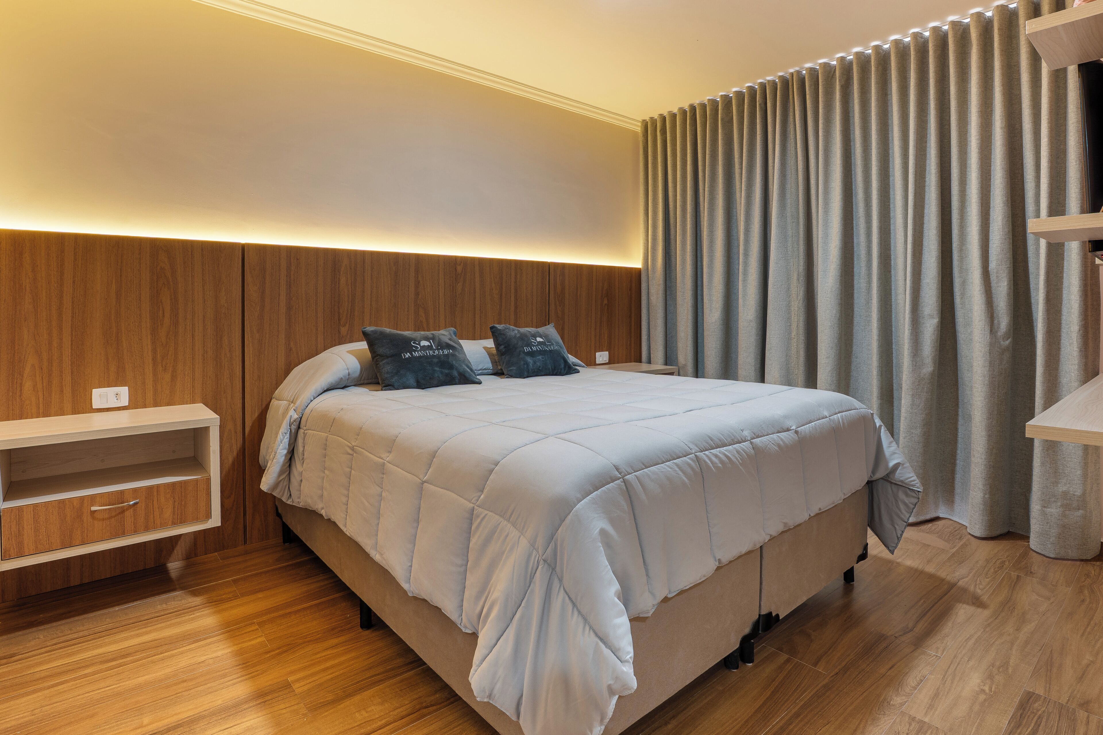Quarto com cama, cabeceira de madeira, mesa de cabeceira e prateleira embutida.