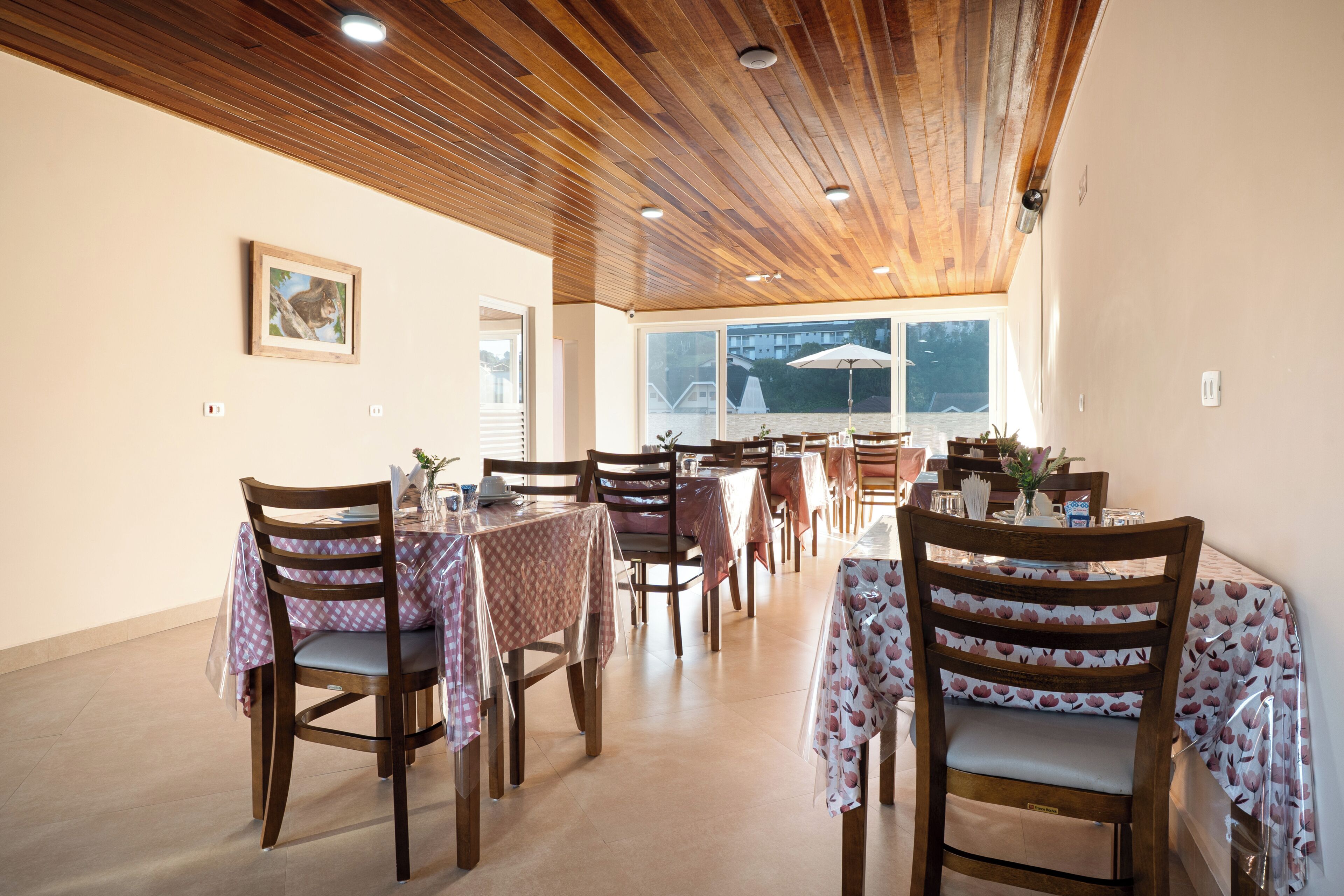 A dining area with wooden ceiling, tables with patterned tablecloths, and chairs.